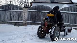 Бульдозер из мотоблока с передним адаптером чистит снег.