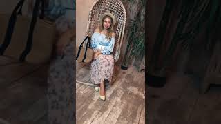 БЛУЗА СО СПУЩЕННЫМИ ПЛЕЧАМИ, ЮБКА ПЛИССИРОВАННАЯ В ЦВЕТОЧЕК, ШЛЯПКА ПЛЕТЕНАЯ С ЧЕРНОЙ ЛЕНТОЧКОЙ