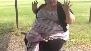 A fat woman riding a kids wheeled scootie